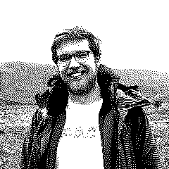Me grinning at the camera wearing a unzipped jacket in a moor. The image is dithered and toned to match the rest of the site